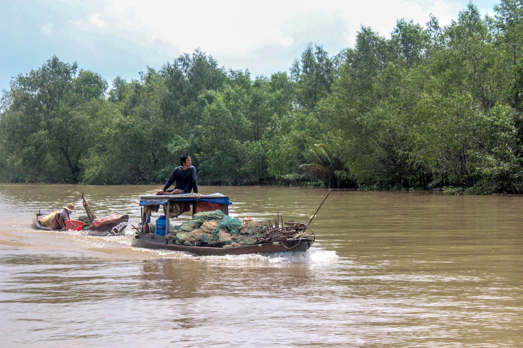 Can Tho Mekong — A man navigates a wooden boat on the Mekong River in Vietnam, surrounded by lush
