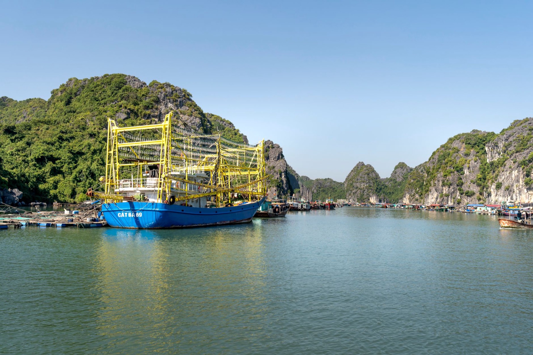 Cat Ba — A vibrant fishing boat moored in a picturesque Vietnamese harbor, surrounded by