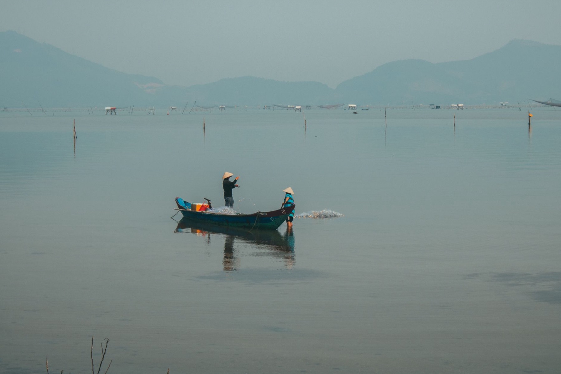 Con Dao — Fishermen on a boat in the serene waters of Hue, Vietnam, casting nets at dawn.
