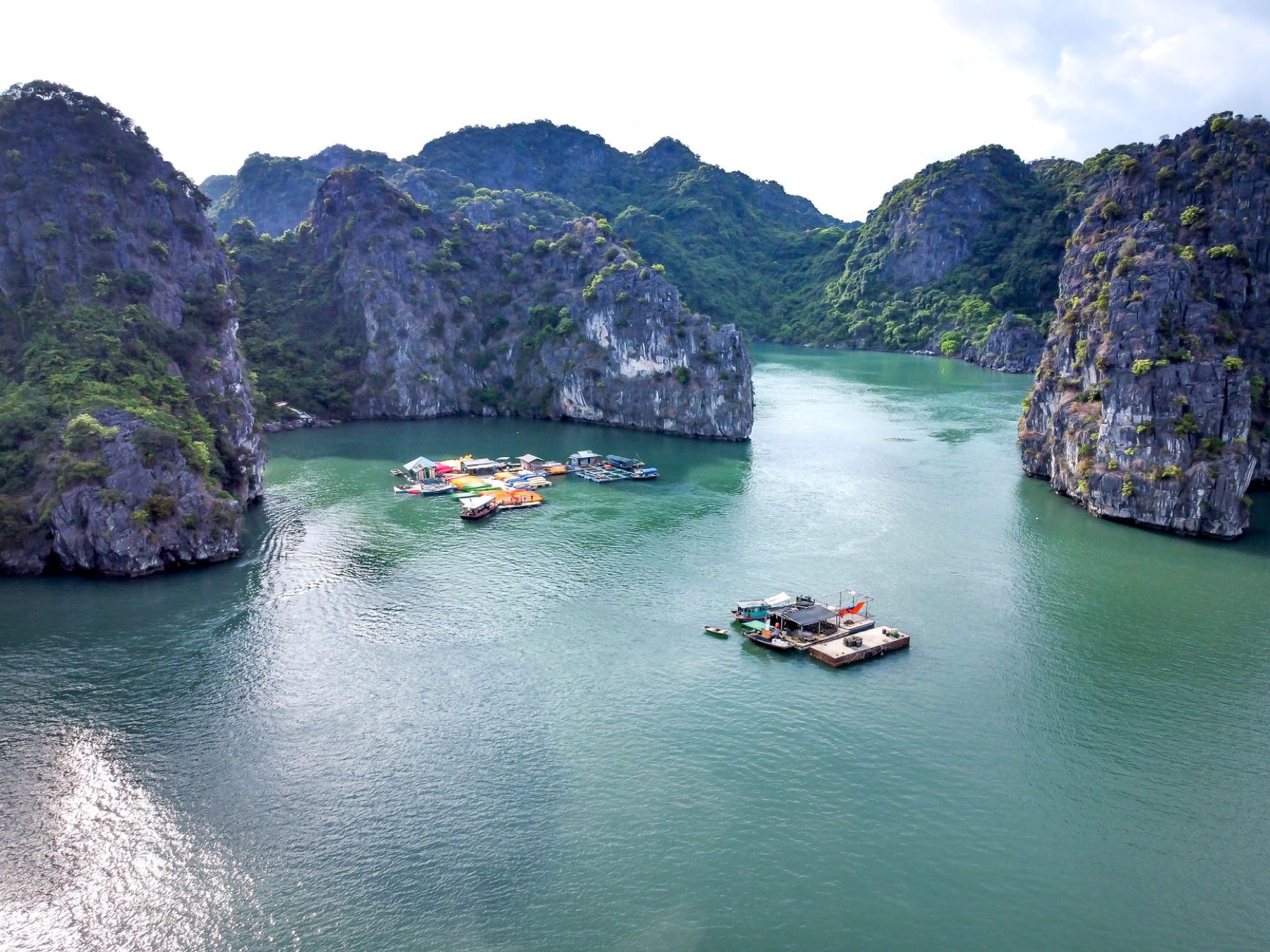 Ha Long Bay — Scenic aerial view of boats in a tranquil bay surrounded by limestone cliffs.