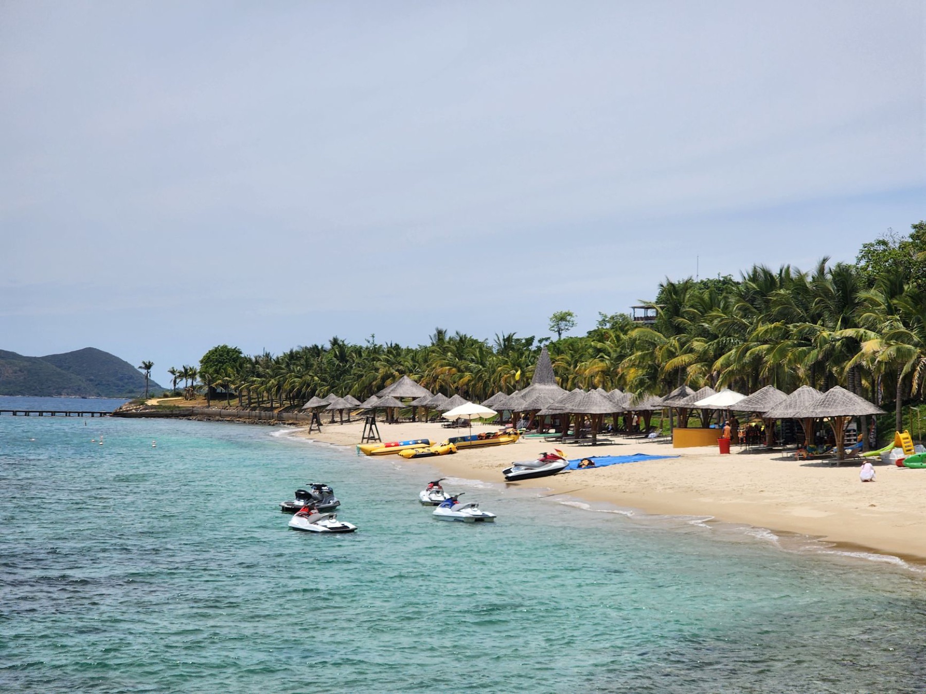 Nha Trang — A serene tropical beach with jet skis, palm trees, and thatched umbrellas along
