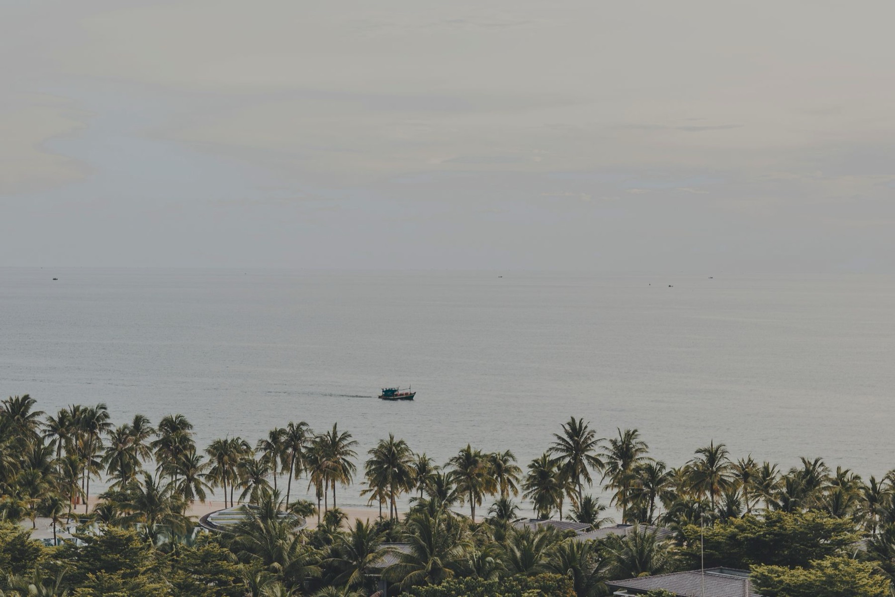 Phu Quoc — Serene panorama of palm-lined Phu Quoc beach with a distant boat on the calm sea