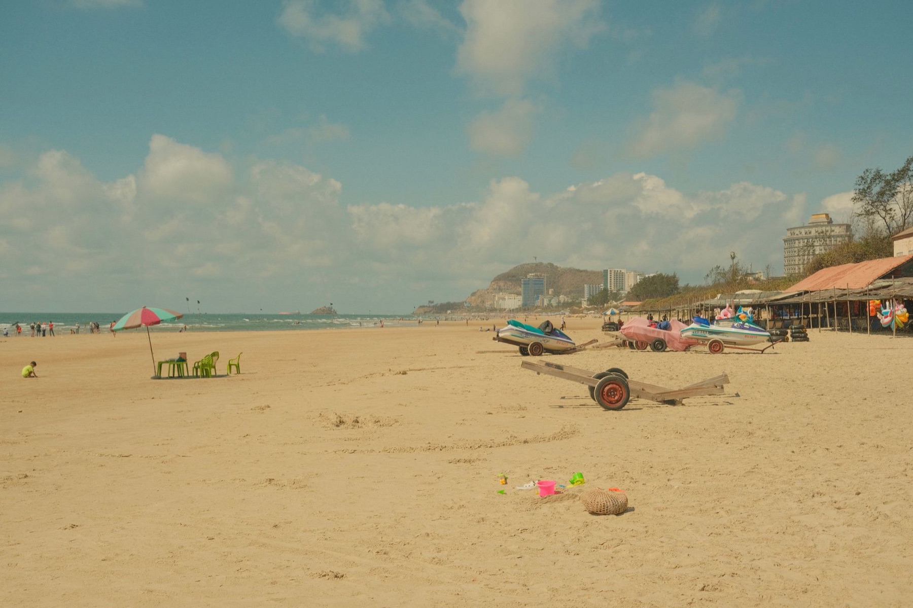 Vung Tau — Serene sandy beach with colorful parasol and beached boats, under clear sky.