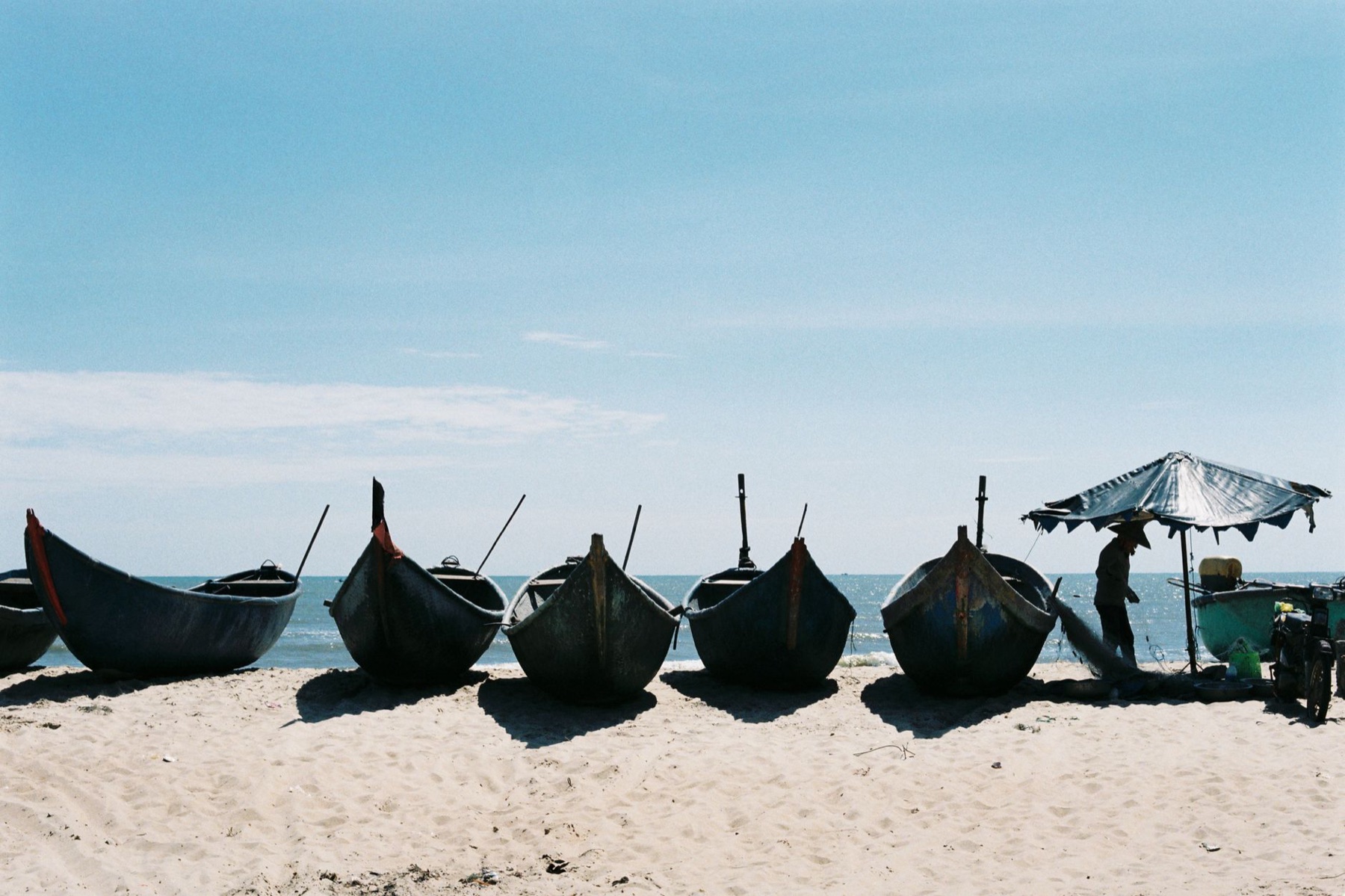 Vung Tau — Fishing boats lined up on a serene beach in Ba Ria, Vietnam under a clear sky.